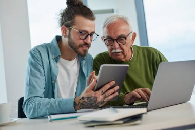Genç bir eğitimci, öğrenci dizüstü bilgisayarında yazarken, bir projeyi tabletinde nasıl çözeceğini gösteriyor..