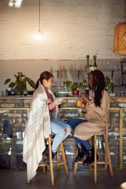 İki çok kültürlü arkadaş kafeteryada oturur, içecek içer ve sohbet ederiz..