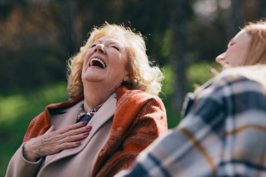 Bir büyükanne parkta bankta otururken ergen torunuyla gülüp eğleniyor..