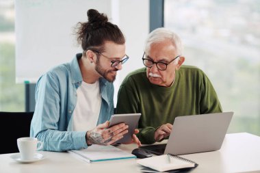Genç bir eğitimci, öğrenci dizüstü bilgisayarında yazarken, bir projeyi tabletinde nasıl çözeceğini gösteriyor..