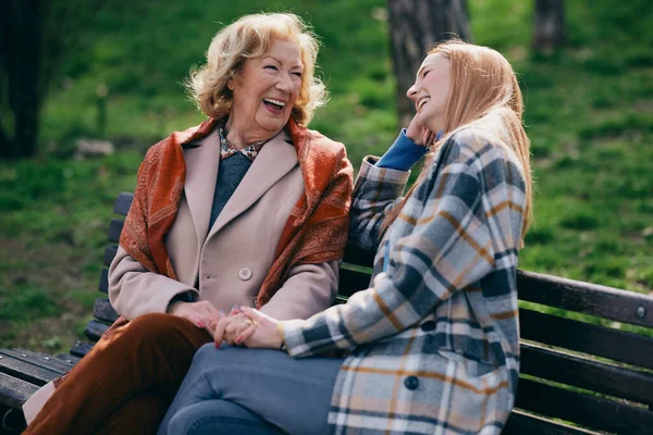 Bir büyükanne parkta bankta otururken ergen torunuyla gülüp eğleniyor..