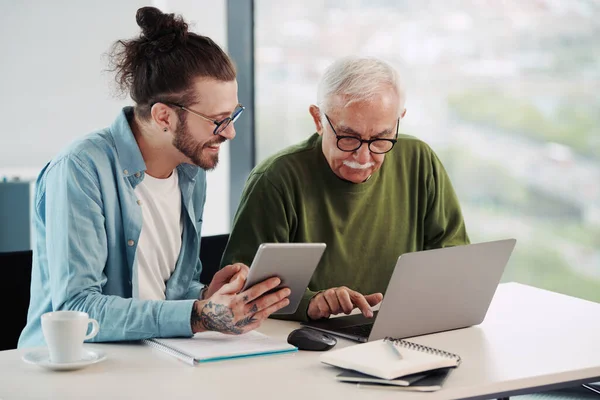 Young educator showing senior student how to solve a problem on project on his tablet while the student looking at the tablet.