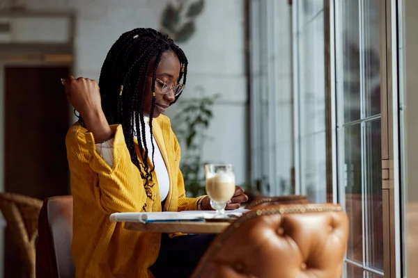 Zeki bir Afrikalı kız bir kafede oturur ve ders kitabına ödevlerini yazar..