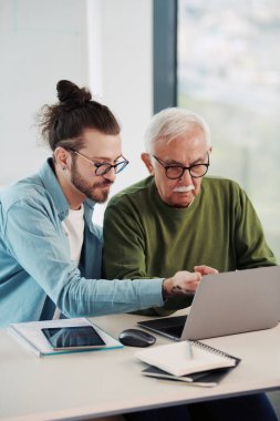 Genç bir eğitimci, öğrenci dizüstü bilgisayarında yazarken, bir projeyi tabletinde nasıl çözeceğini gösteriyor..