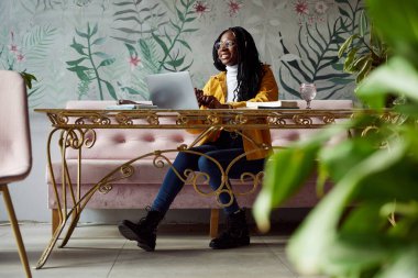 Gülümseyen Afrikalı bir üniversiteli kız bir kafede oturur ve dizüstü bilgisayarıyla okul projesini bitirir..