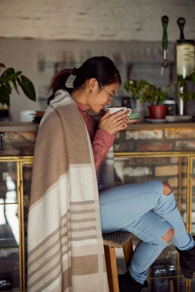 An asian young woman is sitting in a bar and smelling fresh morning coffee.