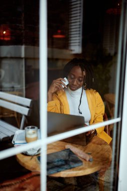 Kafeteryada oturan Afrikalı bir kız ve kredi kartını bilgisayarda online alışveriş için kullanıyor..