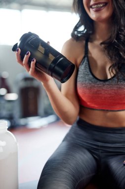Formda bir sporcu kadın protein tozunu karıştırıyor ve spor salonunda protein içeceği yapıyor..