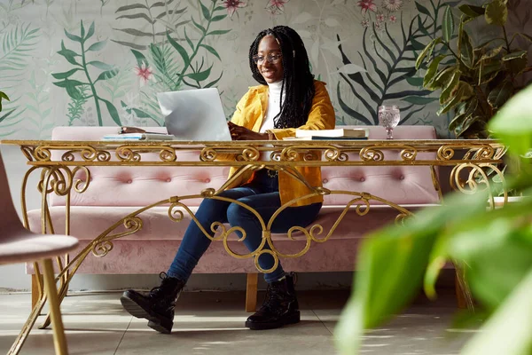 Kafeteryadaki laptopuyla okul ödevini yapan neşeli, genç Afrikalı kadın..