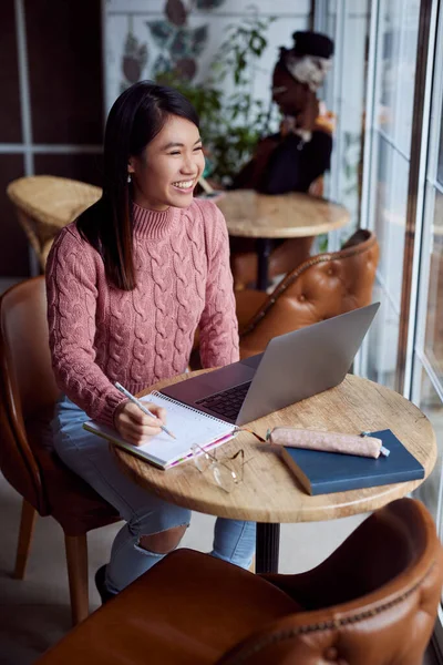 An Asian girl follows online lectures on the laptop at a cafe.