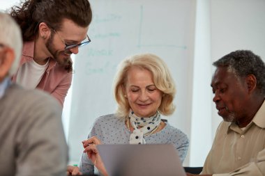 Elinde tablet tutan genç bir eğitimci ve çok kültürlü son sınıf öğrencilerine web tasarımı yapmayı öğretiyor..