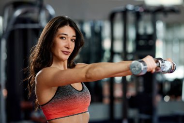 Formda, kaslı bir sporcu spor salonunda dambıllarla egzersiz yapıyor..