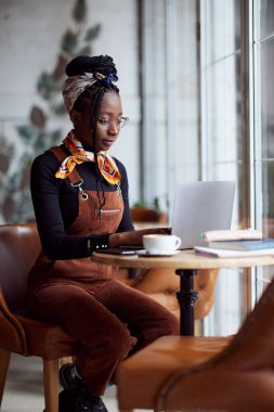 Kafeteryadaki laptopuyla okul ödevini yapan Afrikalı genç bir kadın..