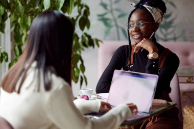 İki çok kültürlü kız öğrenci bir dizüstü bilgisayarla okul projesi yapıyor..