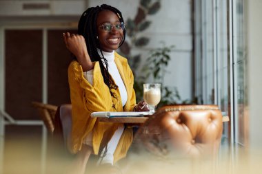 Çok ırklı mutlu bir kız öğrenci kameraya gülümserken okul ödevini bir kitaba yazıyor..