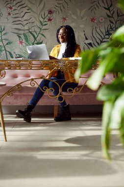 Irklar arası üniversiteli bir kız bir kafede oturuyor ve laptopuyla kompozisyonunu bitiriyor..