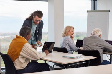 Çok kültürlü bir grup yaşlı öğrenci sınıftaki genç eğitmenleriyle bir ödevi tartışıyor..