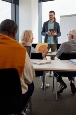 Genç hipster öğretmeni sınıftaki sosyal medya hakkında çok kültürlü bir grup üst düzey insanı eğitiyor..