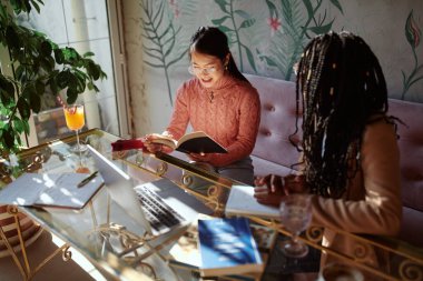 Çok kültürlü bir bayan öğrenci kafeteryada oturmuş kompozisyon üzerinde çalışıyor..