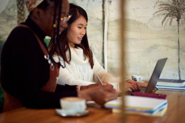 Kafeteryada oturan ve sınava çalışan iki çok kültürlü kız öğrenci..