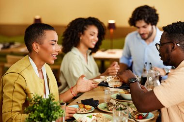 A multicultural group of friends is having dinner in the restaurant.
