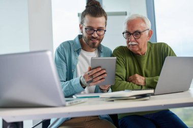 Genç bir eğitimci, öğrenci dizüstü bilgisayarında yazarken, bir projeyi tabletinde nasıl çözeceğini gösteriyor..