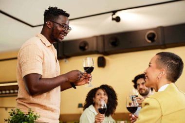 Afrikalı bir adam bir restoranda elinde bir bardak şarapla arkadaşlarıyla kadeh kaldırmayı teklif ediyor..