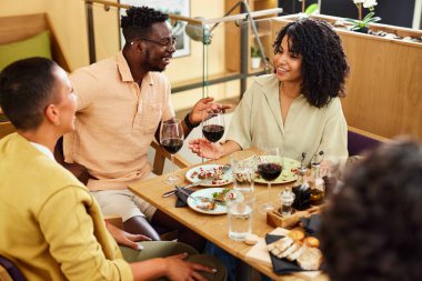 A group of multicultural friends is enjoying dinner and chatting in a restaurant.