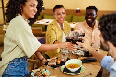 The interracial friends are toasting with wine in a restaurant.