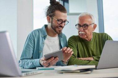 Genç bir eğitimci, öğrenci dizüstü bilgisayarında yazarken, bir projeyi tabletinde nasıl çözeceğini gösteriyor..