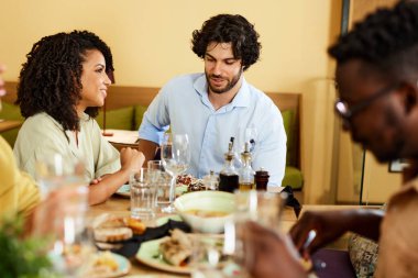 A happy couple is sitting in a restaurant with friends, eating dinner and chatting.