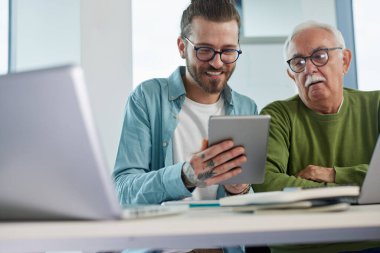 Genç bir eğitimci, öğrenci dizüstü bilgisayarında yazarken, bir projeyi tabletinde nasıl çözeceğini gösteriyor..