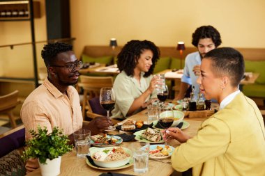 Dört arkadaş restoranda oturmuş şarap içiyor, konuşuyor ve akşam yemeğinin tadını çıkarıyorlar..