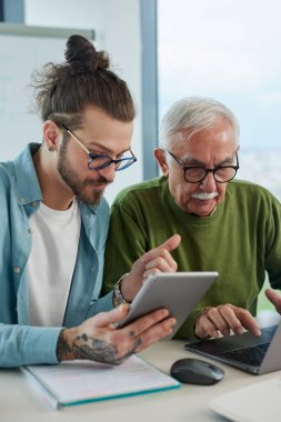Genç bir eğitimci, öğrenci dizüstü bilgisayarında yazarken, bir projeyi tabletinde nasıl çözeceğini gösteriyor..