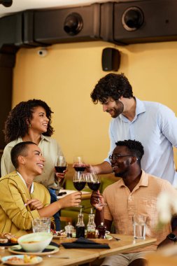 A cheerful group of friends in a winery toast with red wine and have fun.