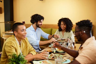 Çok kültürlü arkadaşlar bir restoranda oturup yemek yiyor ve konuşuyorlar..