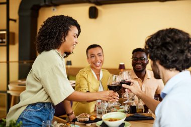 Interracial friends are toasting for success in a restaurant with red wine.