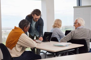 A group of senior students sit in a classroom with their teacher and work on a school project.