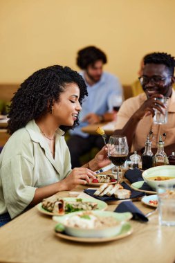 Bir kadın, arkadaşlarıyla yemek masasında otururken restoranda yemek yiyor..