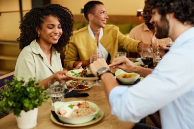 A small interracial group of friends is sitting in a restaurant and having dinner.
