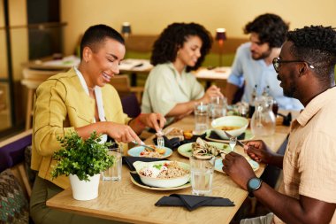 Çok kültürlü arkadaşlar bir restoranda oturup yemek yiyor ve konuşuyorlar..