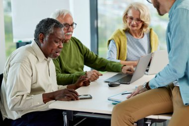 Genç hipster eğitimcisi sınıflarda teknoloji ve internet kullanan üst düzey çok ırklı insanlara ders veriyor..