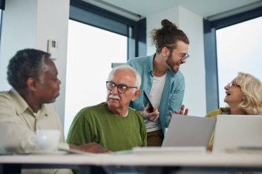 Genç hipster eğitimcisi sınıflarda teknoloji ve internet kullanan üst düzey çok ırklı insanlara ders veriyor..
