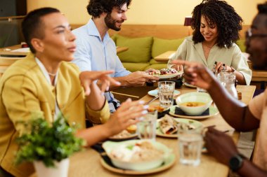 Group of multicultural friends sit in a restaurant, eating dinner an talking.