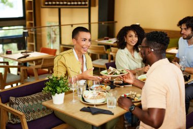 A group of friends sits at the dinner table at the restaurant, eating dinner, having fun, and laughing.