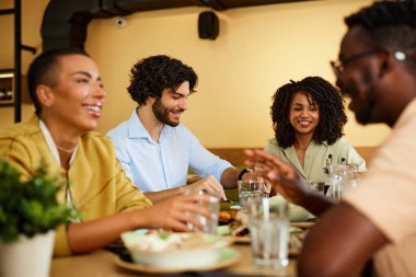 Multicultural friends are sitting in a restaurant, eating food and talking.
