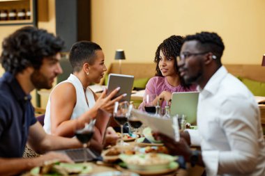 Busy businesspeople sit at the dinner table in a restaurant, working on laptops and having an important meeting.