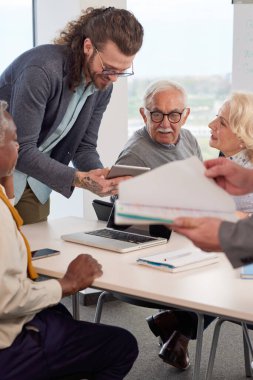 Genç hipster eğitimcisi sınıflarda teknoloji ve internet kullanan üst düzey çok ırklı insanlara ders veriyor..