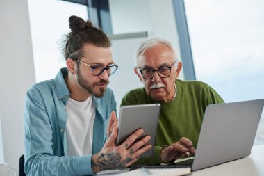 Genç bir eğitimci, öğrenci dizüstü bilgisayarında yazarken, bir projeyi tabletinde nasıl çözeceğini gösteriyor..