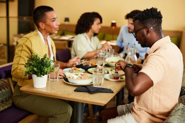 Arkadaşlar bir restoranda yemek masasında oturur, yemek yer ve sohbet ederler..
